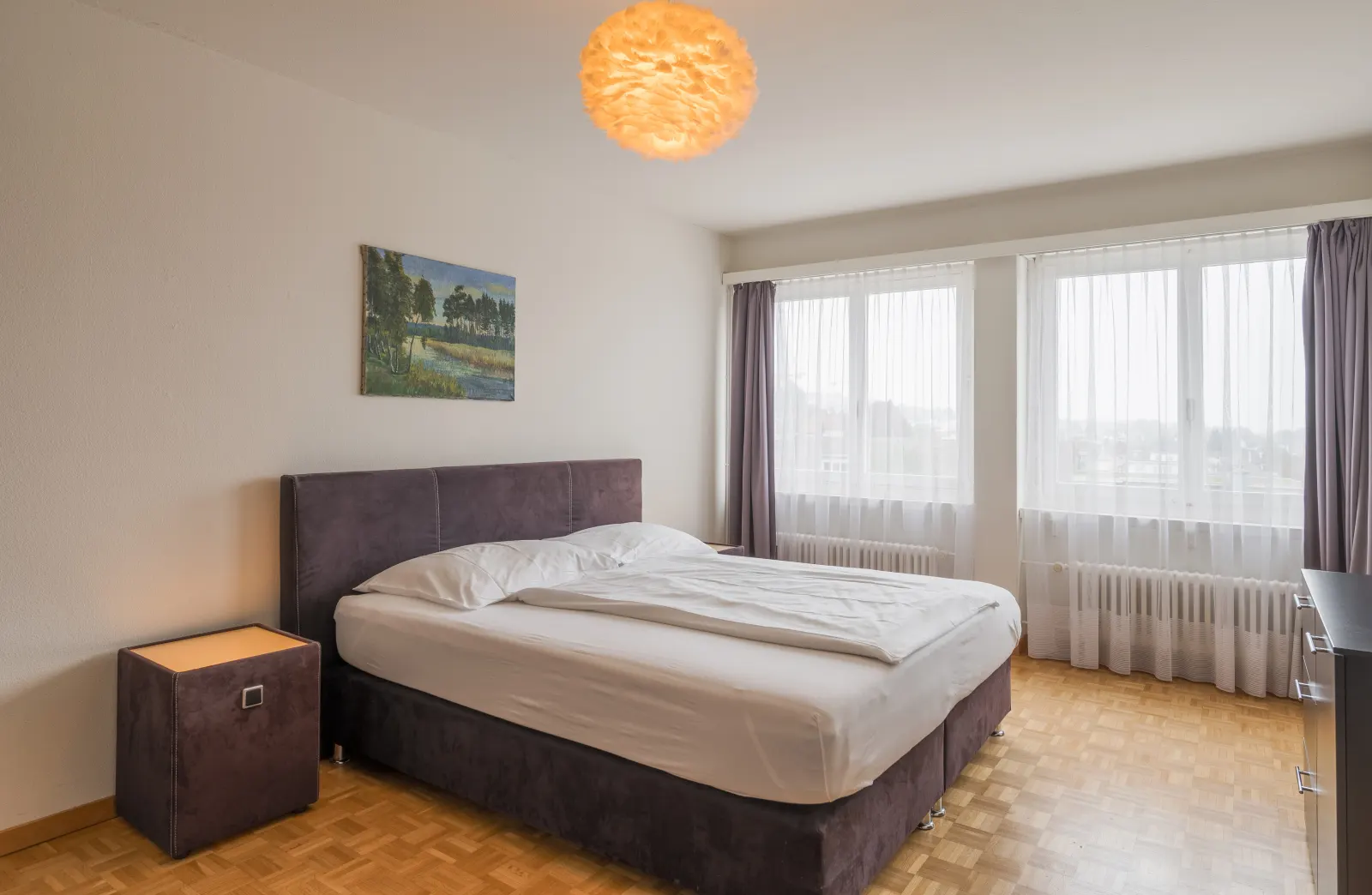 Schlafzimmer mit Doppelbett, Nachttisch und Fenstern über Eck